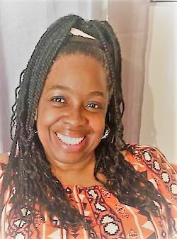 Cathy Peters, smiling, with long braided hair and wearing a patterned orange top