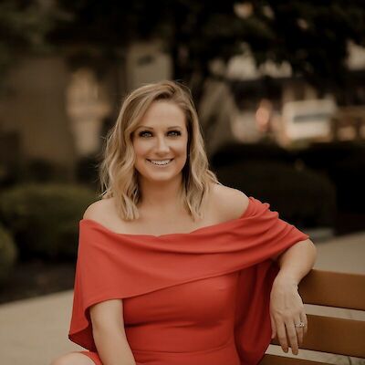 Chelsea Ohlemiller, smiling, seated outdoors on a bench in a red off-the-shoulder dress