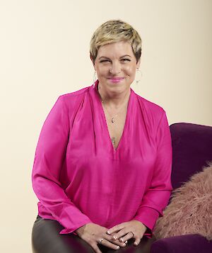 Amy Fabian-Crump, smiling, seated and wearing a bright pink blouse