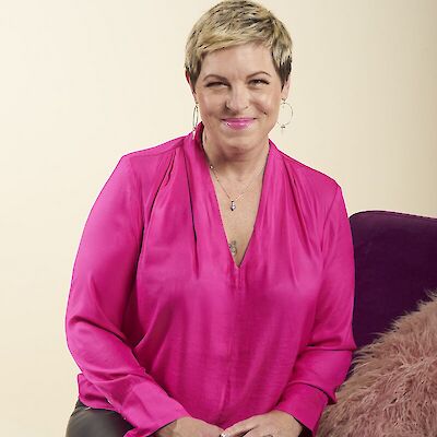 Amy Fabian-Crump, smiling, seated and wearing a bright pink blouse