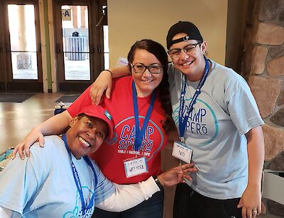 Three smiling Camp Spero volunteers in matching t-shirts, arms around each other