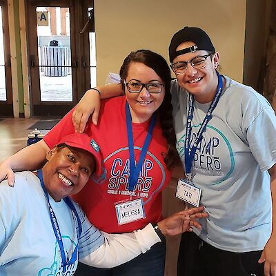 Three smiling Camp Spero volunteers in matching t-shirts, arms around each other