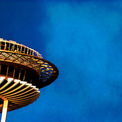 The top of Seattle's Space Needle, its saucer-shaped observation deck lit gold against a deep blue sky