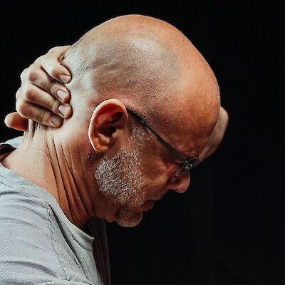 A side profile of a man looking downward while gripping the back of his neck in tension, representing the physical toll and bodily strain that comes from suppressing emotions during grief.