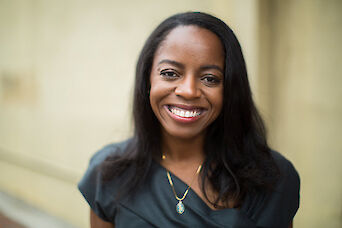 Zeena Regis, smiling, in a dark green top, photographed outdoors