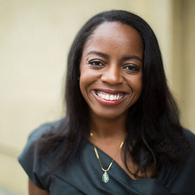 Zeena Regis, smiling, in a dark green top, photographed outdoors