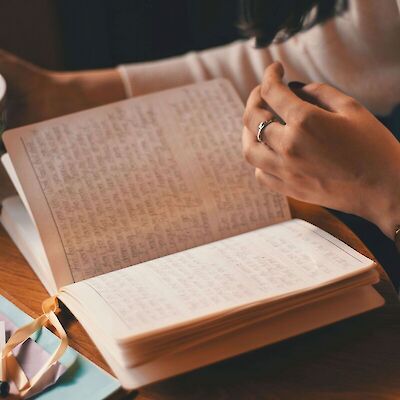 A close-up of a person&rsquo;s hands resting on an open handwritten journal next to a warm cup of tea on a wooden table, taking time for quiet reflection during the grieving process.