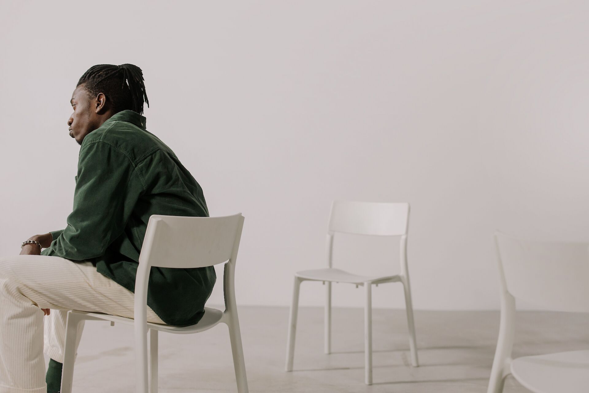 A man sitting alone on a white chair looking to the side, coping with the loss of his wife and life partner.