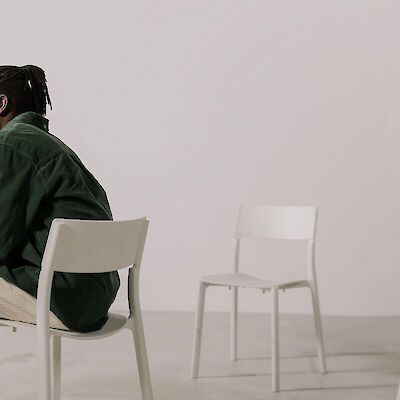 A man sitting alone on a white chair looking to the side, coping with the loss of his wife and life partner.