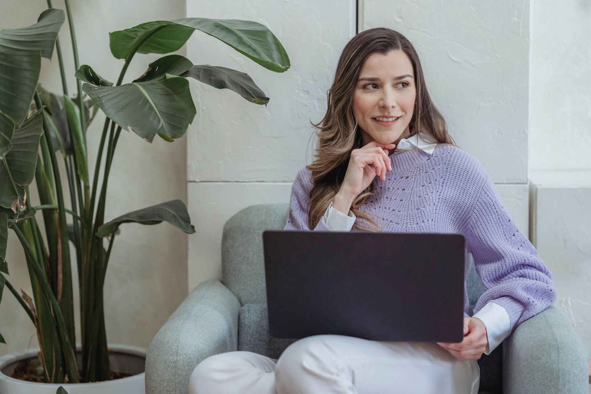 A thoughtfully smiling professional sitting in a chair with a laptop, representing a benefits leader utilizing Help Texts for personalized grief resource matching.
