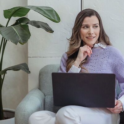 A thoughtfully smiling professional sitting in a chair with a laptop, representing a benefits leader utilizing Help Texts for personalized grief resource matching.