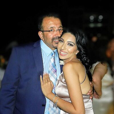 Sarah Khatau, in a satin dress, smiling and embracing her father, who wears a navy suit and tie, at an evening event