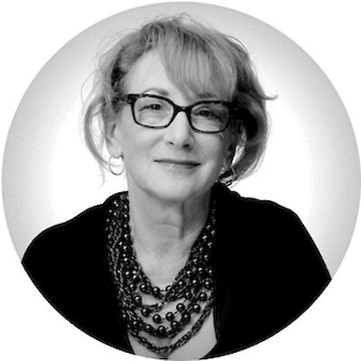 Black-and-white headshot of a smiling woman with glasses and a layered beaded necklace